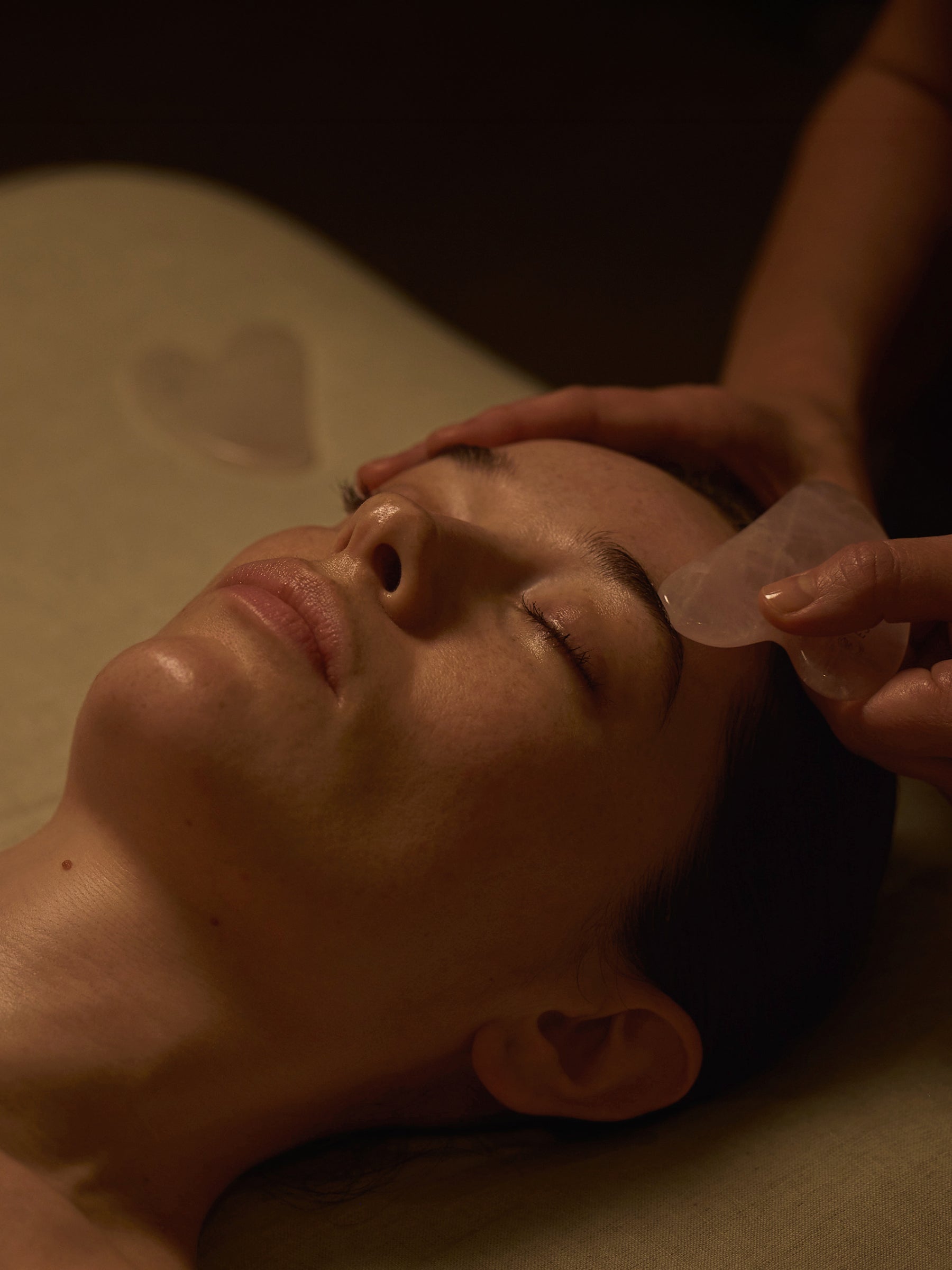 Model laid on therapist bed with therapist applying guq sha to temple