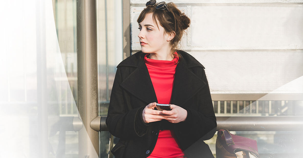 Young woman on phone at a bus stop.