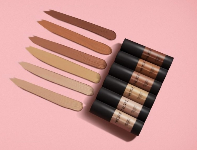 Swatches of different foundation shades against a pink background